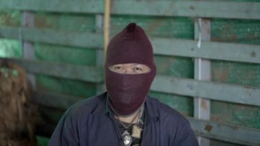 Yaşlı Taylandlı adam geleneksel bir fabrikada şapka takarken kameraya bakıyor.