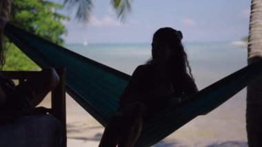 Tayland 'da tropik plajda salıncakta sallanan tanınmayan bir kadının arka görüntüsü - 4K Yatay Video