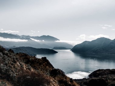Etkileyici mavi gölün manzarası bitki örtüsü ile kayalık büyük dağlar arasındaki sakin sular bulutlar, dağ zirvesi ve Yeni Zelanda ile dolu gökyüzü altında güzel bir doğal ortam.