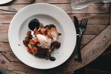 Kızarmış domuz pastırması ve fındıklı doyurucu bir kahvaltı yanında çatal, bıçak ve yuvarlak ahşap bir masada bir şişe su, Mylk barı, Yeni Zelanda -