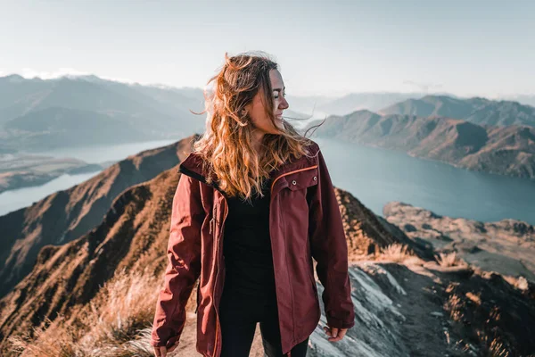 Sarışın, beyaz saçlı, neşeli ve mutlu bir genç kız dağın tepesinden gülüyor, doğanın en güzel manzarasıyla eğleniyor, Roys Peak, Yeni Zelanda - seyahat konsepti