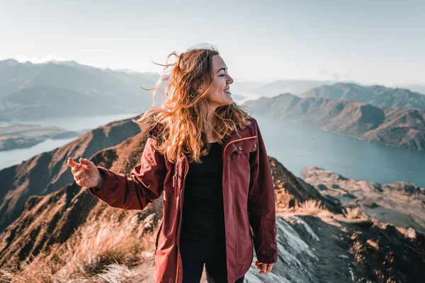 Kafkasyalı, uzun sarı saçlı genç bir kadın kameraya bakıp gülümsüyor. Doğanın ortasında, sakin ve sakin bir yerde, Roys Peak, yeni bir yerde.