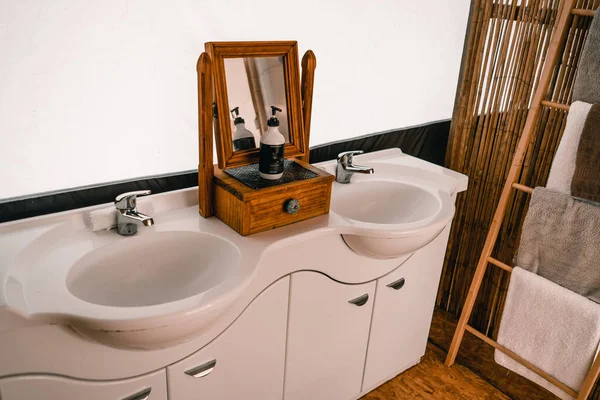 pair of porcelain sink faucets mirror and wooden vanity next to soap dish and clean towels in a tent bathroom - Lifestyle travel concept