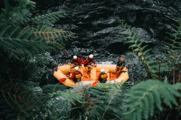 Aerial view of five people wearing swimsuits and life jackets with oars in hand inside an inflatable boat ready to go rafting on the strong current of the river in Okere, new zealand - Nature concept
