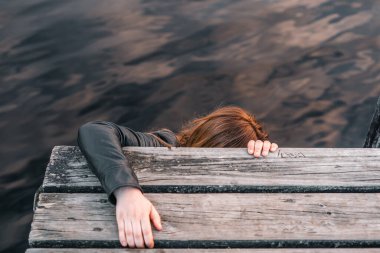 Kafkasyalı kızıl saçlı bir kız iskelede tahta levhalara tutunarak göl suyundan, Matheson gölünden, Yeni Zelanda 'dan tırmanmaya çalışıyor.