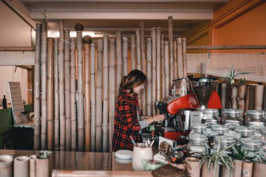 Büyük bambu kamışlarıyla temiz ve derli toplu kahve dükkanı ve ekose gömlekli Asyalı kız kahvaltı için lezzetli latte hazırlarken kahve makinesini manipüle ediyorlar, Mylk barı, Yeni Zelanda - yaşam tarzı konsepti