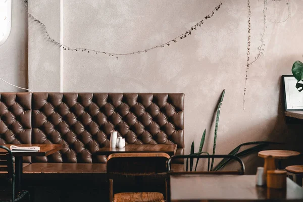Sessiz ve dost canlısı bir kahve dükkanındaki ahşap masaları, Mylk Bar 'ı, Yeni Zelanda' daki yaşam tarzı konseptini, eski moda rahat deri koltuğun üzerinde asılı şirin yapraklı bitkilerle dolu gri bir duvar.