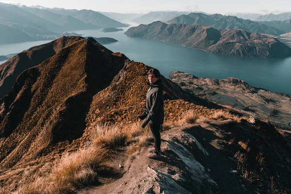 young caucasian woman with blue eyes jacket and black pants with reflex camera hanging from her shoulder calm and relaxed standing on top of a stone to contemplate the landscape of the mountains and