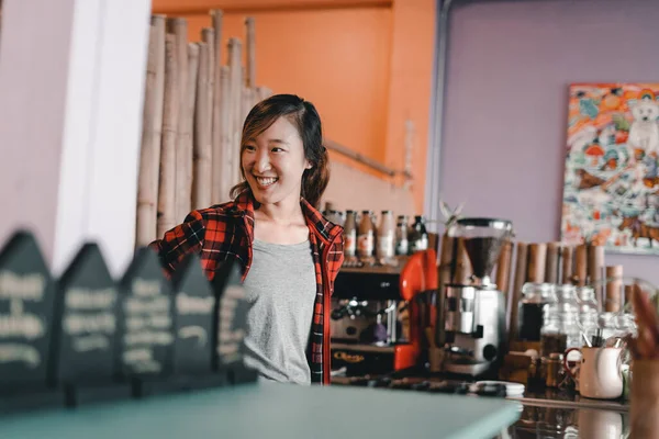 asian girl dressed in a gray t-shirt and checkered shirt happy and with a big smile working by the coffee machine and grinder in a nice coffee shop, the mylk bar, new zealand - Lifestyle concept