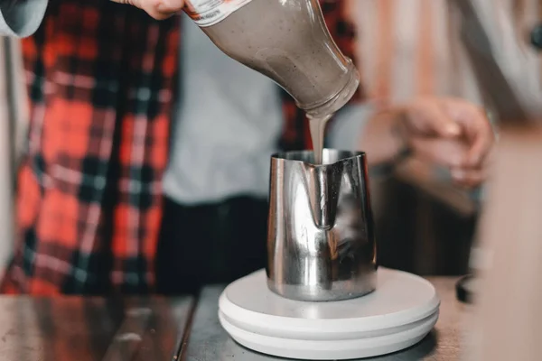 creamy liquid chocolate pouring from a glass bottle into a clean metal container on the small scale, the mylk bar, new zealand - Lifestyle concept