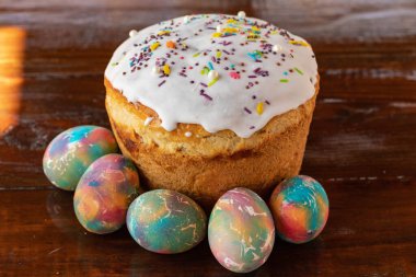 Paskalya pastası ve çok renkli Paskalya yumurtaları. Parlak ambalaj. Paskalya hazırlıkları. Beyaz jöleli şenlikli kekler, şenlikli tahta masa.