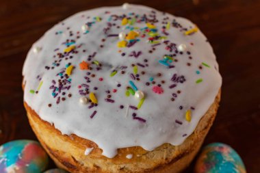 Paskalya pastası ve çok renkli Paskalya yumurtaları. Parlak ambalaj. Paskalya hazırlıkları. Beyaz jöleli şenlikli kekler, şenlikli tahta masa.