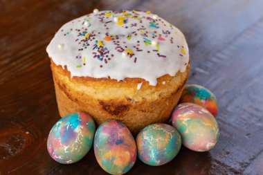 Paskalya pastası ve çok renkli Paskalya yumurtaları. Parlak ambalaj. Paskalya hazırlıkları. Beyaz jöleli şenlikli kekler, şenlikli tahta masa.