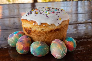 Paskalya pastası ve çok renkli Paskalya yumurtaları. Parlak ambalaj. Paskalya hazırlıkları. Beyaz jöleli şenlikli kekler, şenlikli tahta masa.