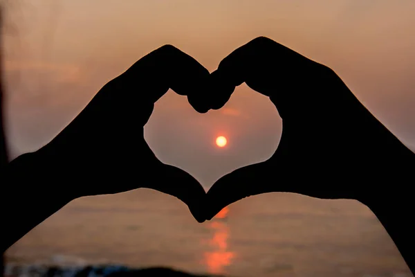 The silhouette made the heart shape from the hands at sunset.