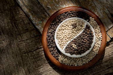 Siyah ve beyaz biber, beyaz üzerine izole edilmiş yin yang şekli eski ahşap bir arka planda..