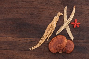 Reishi veya lingzhi mantarı, ginseng, goji üzümü tohumu ve eski ahşap bir arka planda meyan kökü ormanı. Üst görünüm, düz uzanma.
