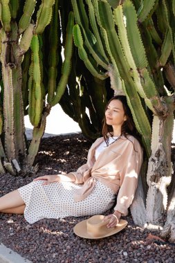 happy woman in skirt sitting in park near giant succulents