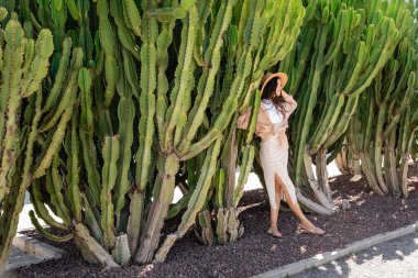 full length of woman in straw hat and skirt near green huge cactuses
