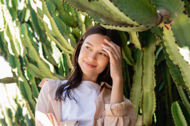 happy brunette woman looking away near giant succulents in park