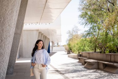 Ceplerinde el ele tutuşan esmer kadın şehir sokağına bakıyor.