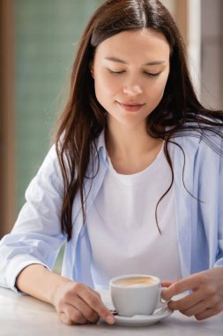 brunette woman sitting with cup of coffee on cafe terrace
