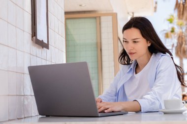 brunette woman in blue shirt working on laptop in street cafe