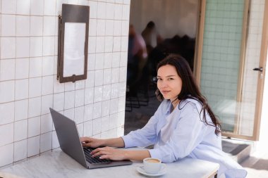 Mutlu kadın yaz terasında dizüstü bilgisayarda yazarken kameraya bakıyor. 