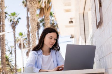 woman sitting on cafe terrace and typing on laptop