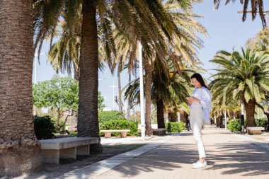 Parktaki Palm alley 'de akıllı telefonlu bir kadının tam boy görüntüsü