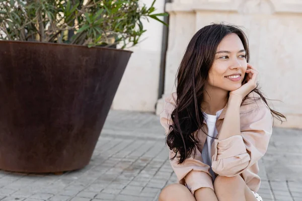 Neşeli kadın büyük bir saksının yanında oturuyor ve başka tarafa bakıyor. 