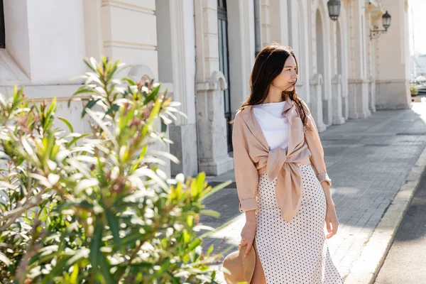 Şık esmer kadın şehir caddesindeki bulanık bitkinin yanından uzağa bakıyor.