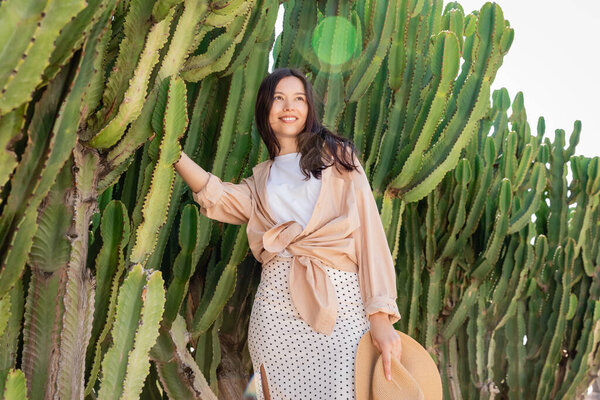 brunette woman in stylish clothes smiling near giant cacti