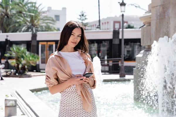 Woman Trendy Clothes Standing Smartphone Blurred Fountain —  Fotos de Stock