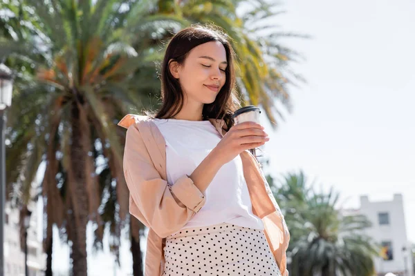 Gülümseyen esmer kadın dışarıda içecek tutuyor.