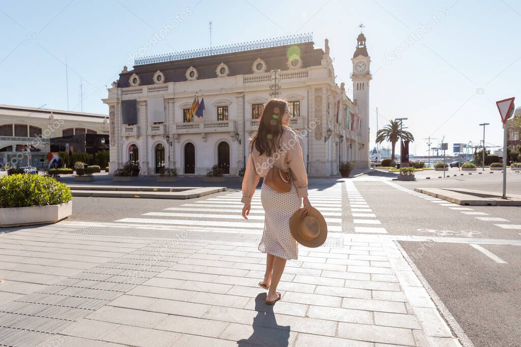 full length of woman walking towards crosswalk on square with clock tower