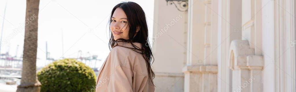 positive brunette woman looking at camera and smiling outdoors, banner