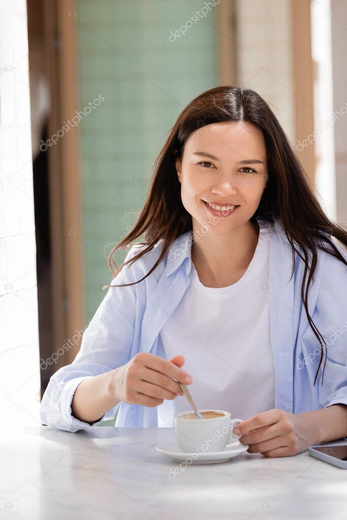 joyful woman smiling at camera near cup of coffee on cafe terrace