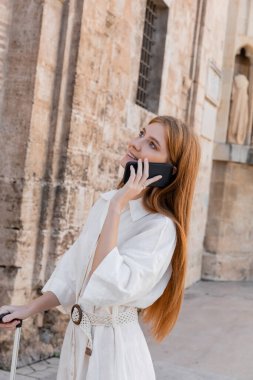 Valencia 'da bavul sapını tutan ve telefonla konuşan neşeli kızıl saçlı kadın.
