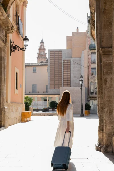 Valizli kızıl saçlı kadının Valencia caddesinde yürüyüşü.