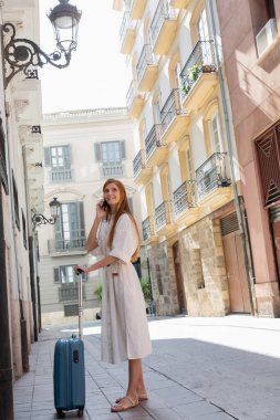 Valencia 'da Avrupa caddesinde bavullu ve akıllı telefondan konuşan mutlu bir kadın. 