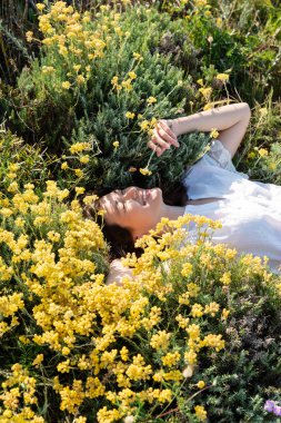 Sarı çiçeklerle çimenlikte uzanan neşeli kadının yüksek açılı görüntüsü 