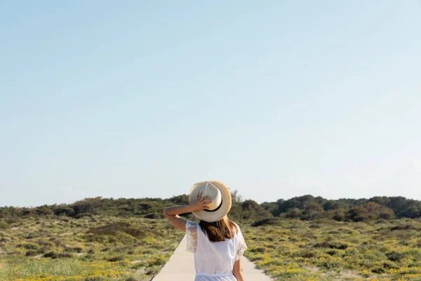 バックビーチでわら帽子を保持ドレスの女性のビュー — ストック写真