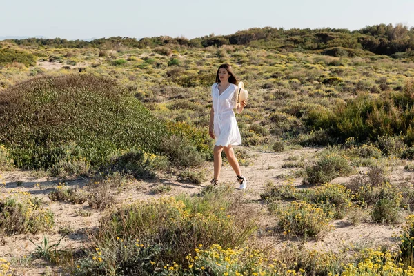 Mujer Morena Vestido Verano Sosteniendo Sombrero Paja Mientras Camina Cerca — Foto de Stock