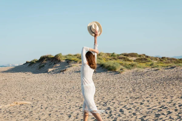 Visão Traseira Mulher Vestido Malha Segurando Chapéu Sol Praia Areia — Fotografia de Stock