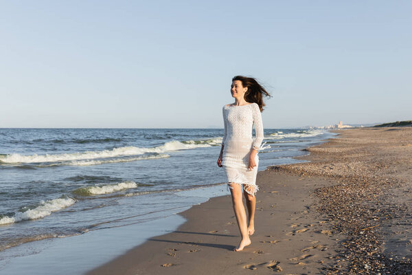 Pretty smiling woman in dress running on beach near sea 