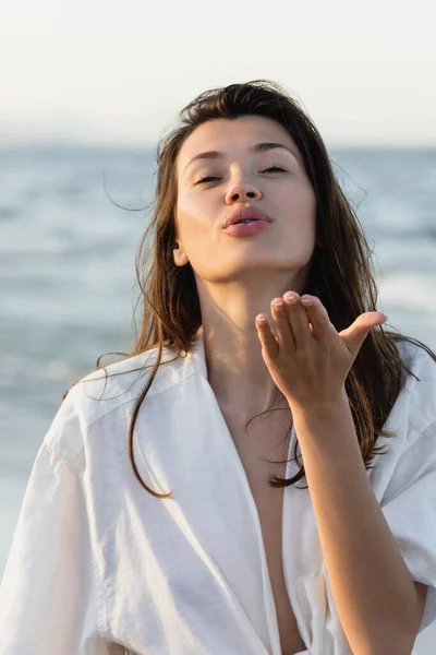 ブルネット女性でシャツ吹いている空気キス近くぼやけた海 — ストック写真
