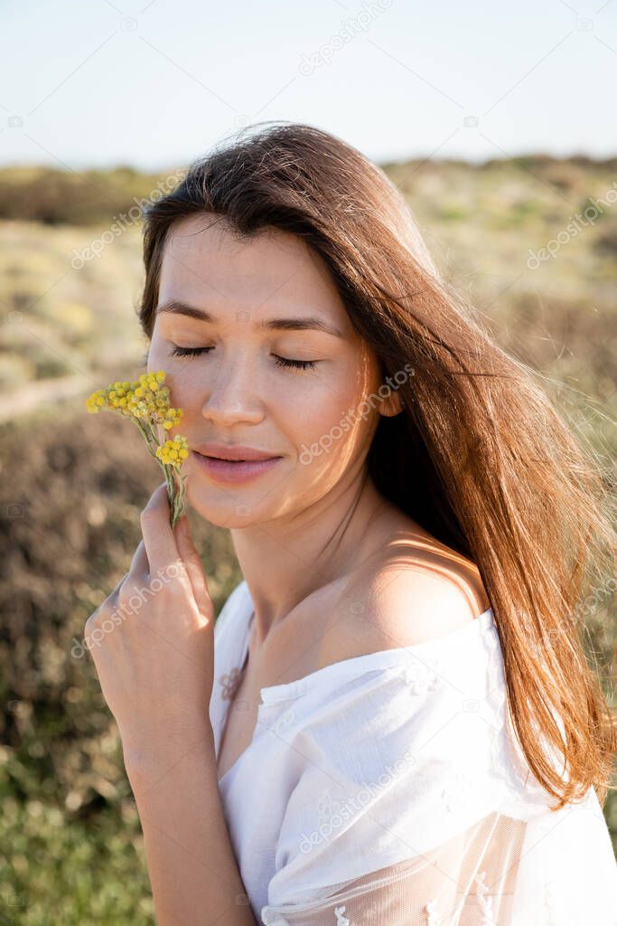 Portrait of woman closing eyes and holding flowers near cheek on beach 