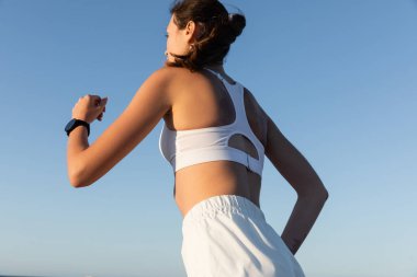 Yazın mavi gökyüzüne doğru koşan genç ve sportif kadının düşük açılı görüntüsü