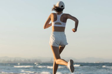 Yazın denize yakın koşan genç ve sportif kadının arka manzarası